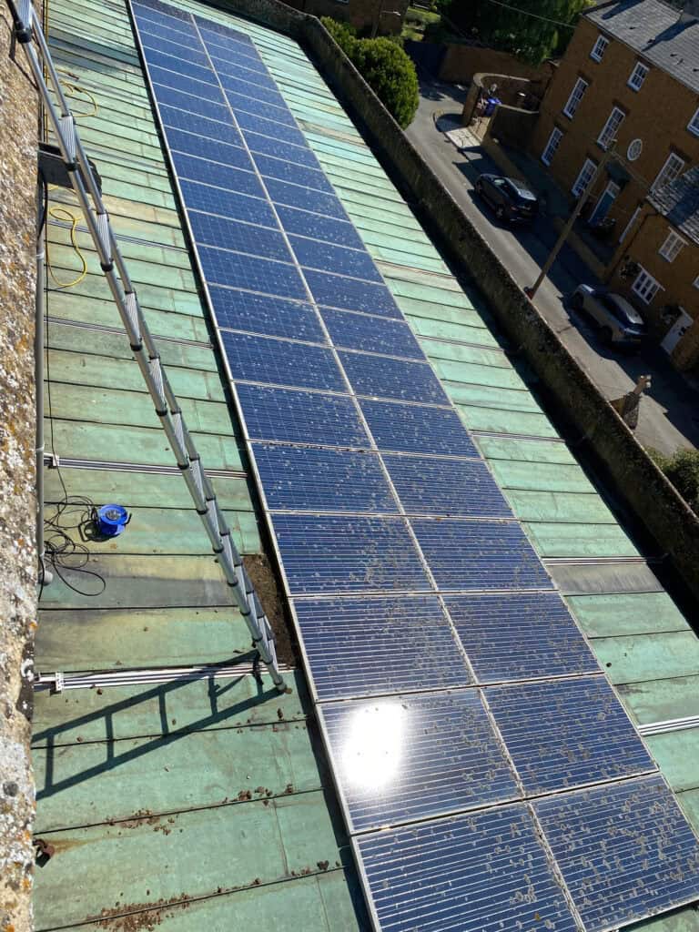 A large array of solar panels (lichen covered) on the roof of a church in Oxfordshire